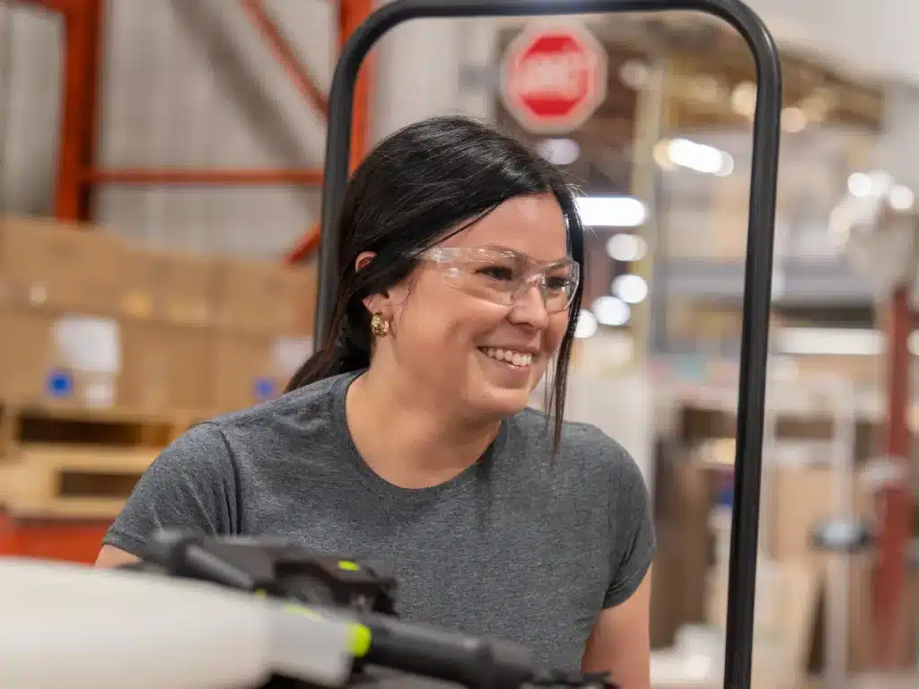 Smiling Innovair employee wearing safety glasses at a workstation on a production line