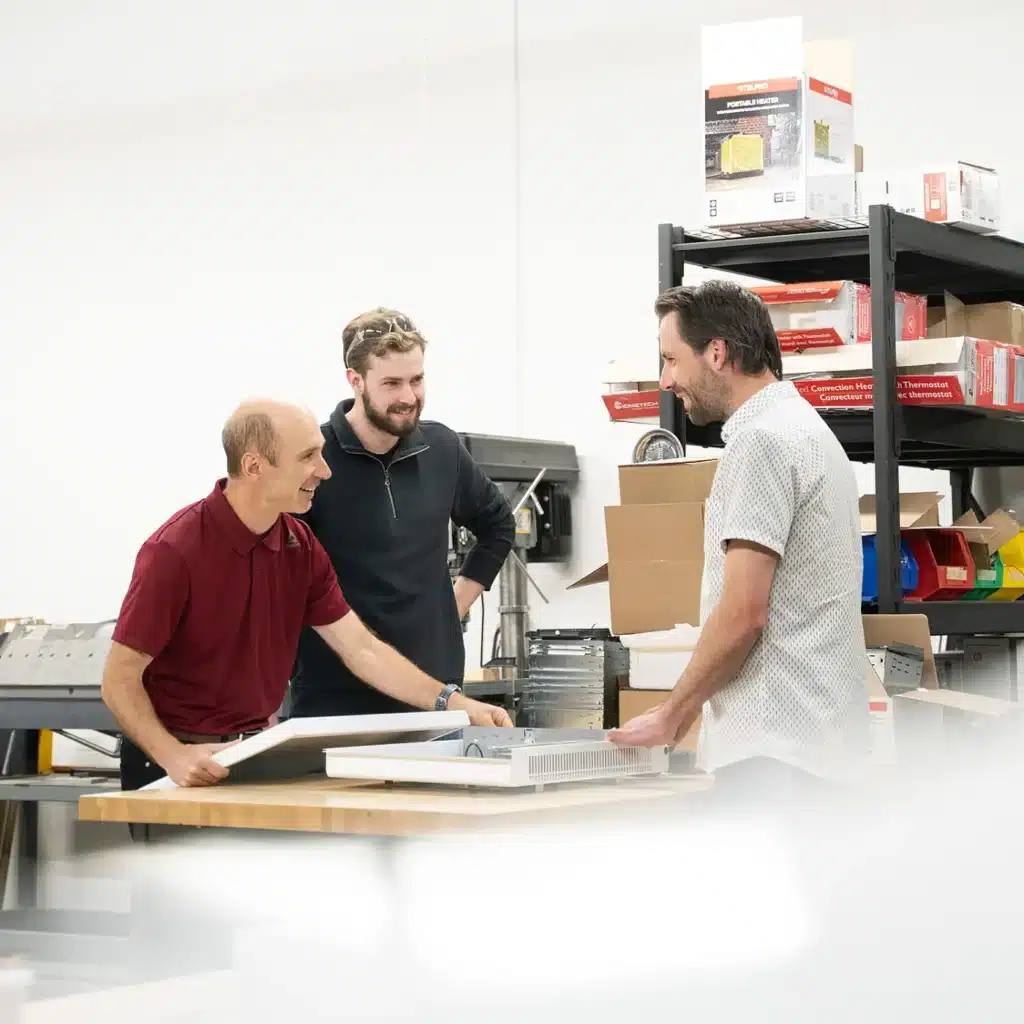 Three Stelpro colleagues examining a convector heater on a workshop bench